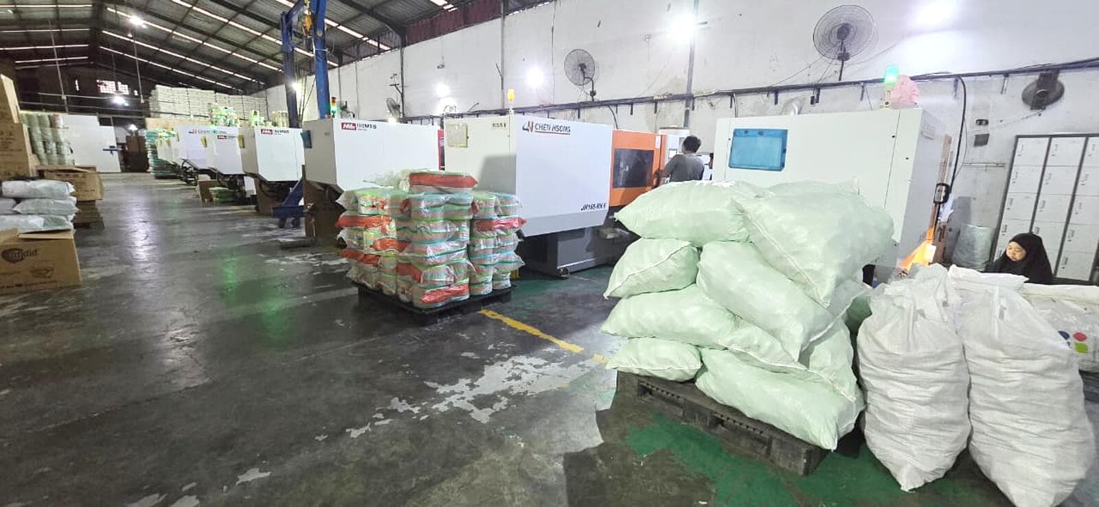 Lantai produksi — mesin injection moulding beroperasi, hasil cetak dikemas di samping mesin